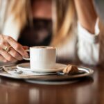 Caffè servito in tazza dopo pranzo, su tavolo con piatto vuoto e posate.