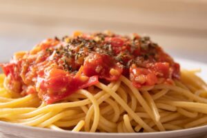 Pasta al pomodoro servita in un piatto, con pomodori freschi e basilico decorativo.